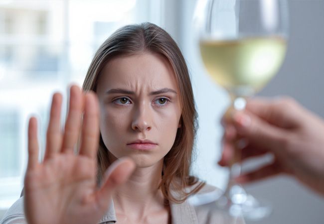 Молодая женщина поднимает ладонь в жесте отказа от бокала белого вина